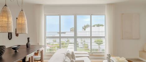 A modern living room with a large window, a dining area, and a sofa.