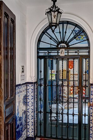 A door with a blue and white patterned tile design, a black metal gate, and a decorative light fixture above it. - Pensión Montoreña (Seville)