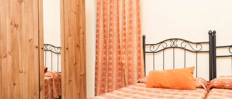 Un dormitorio con un armario de madera, una cama con ropa de cama estampada y una cortina de diseño geométrico.