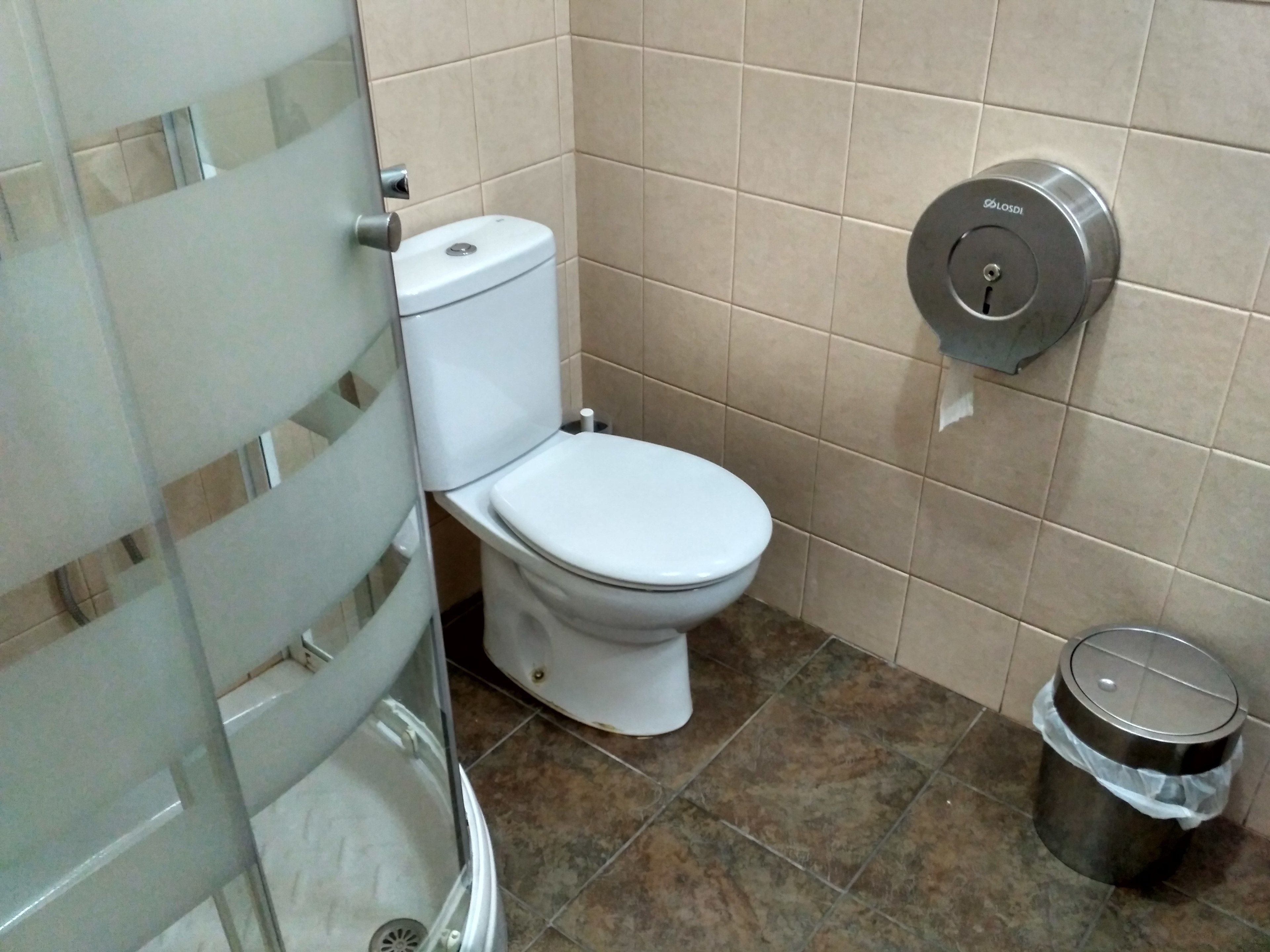Un baño con inodoro, un cubo de basura y un secador de manos.