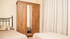 A bedroom with two beds, a wooden wardrobe, and a curtain. - Pensión Montoreña (Seville)