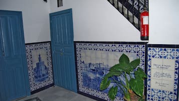 Un pasillo con puertas azules, un muro de azulejos con una escena de río y una planta en maceta.