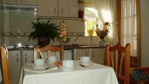 A dining area with a table set for two, a potted plant, and a window with curtains. - Apartamentos Jucar (Tragacete)