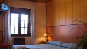 A room with two beds, a television, a window with curtains, and a bedside table with a lamp. - Apartamentos Jucar (Tragacete)