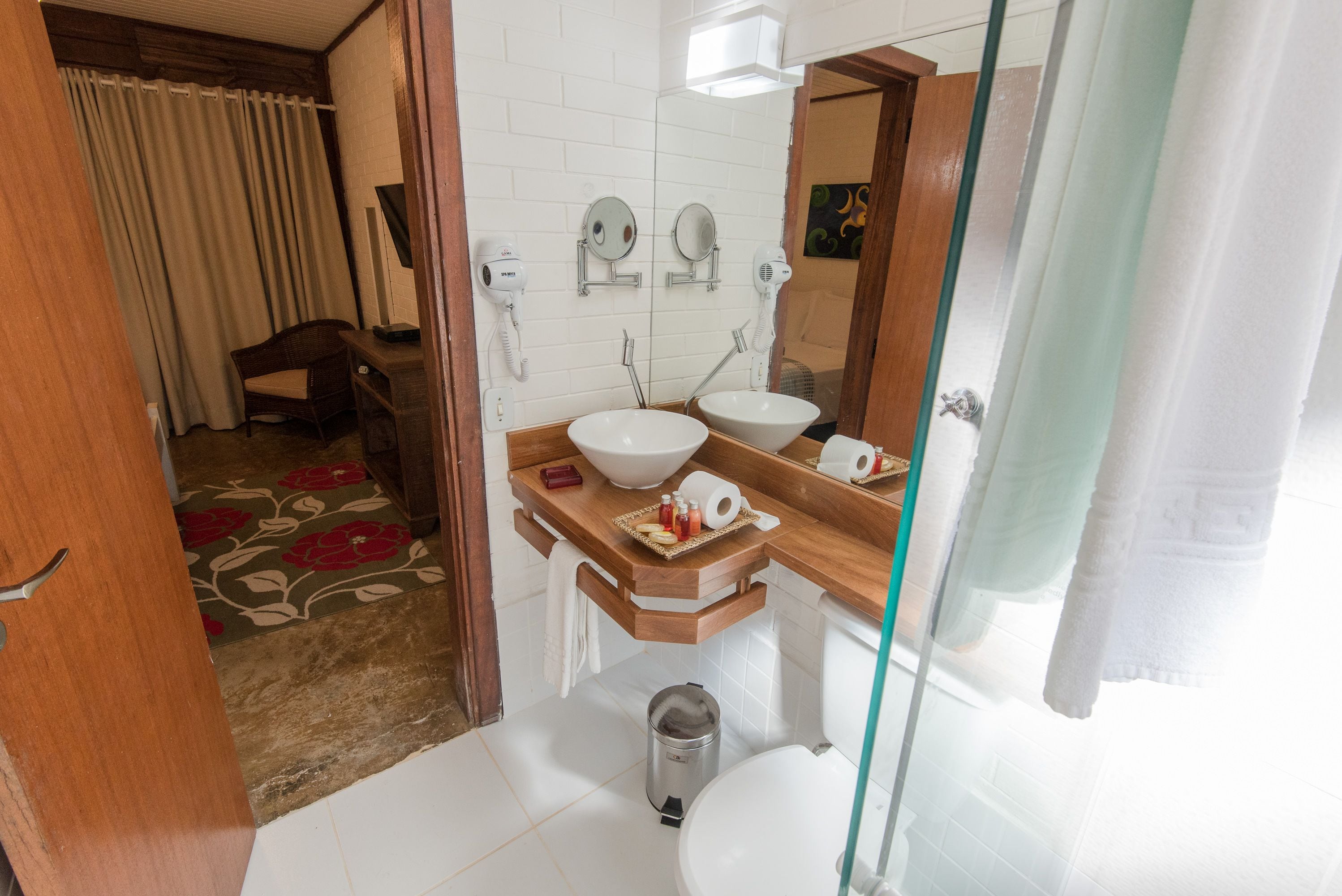 A bathroom with two sinks, a mirror, a hairdryer, and a trash can.