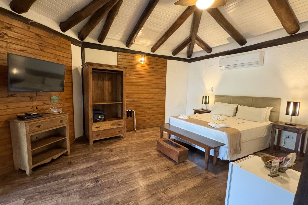 A wooden-floored room with a bed, a TV, a wooden cabinet, and a ceiling fan.