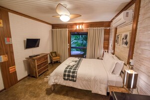 Een slaapkamer met een bed, een televisie, een bureau, een stoel en een raam met gordijnen.