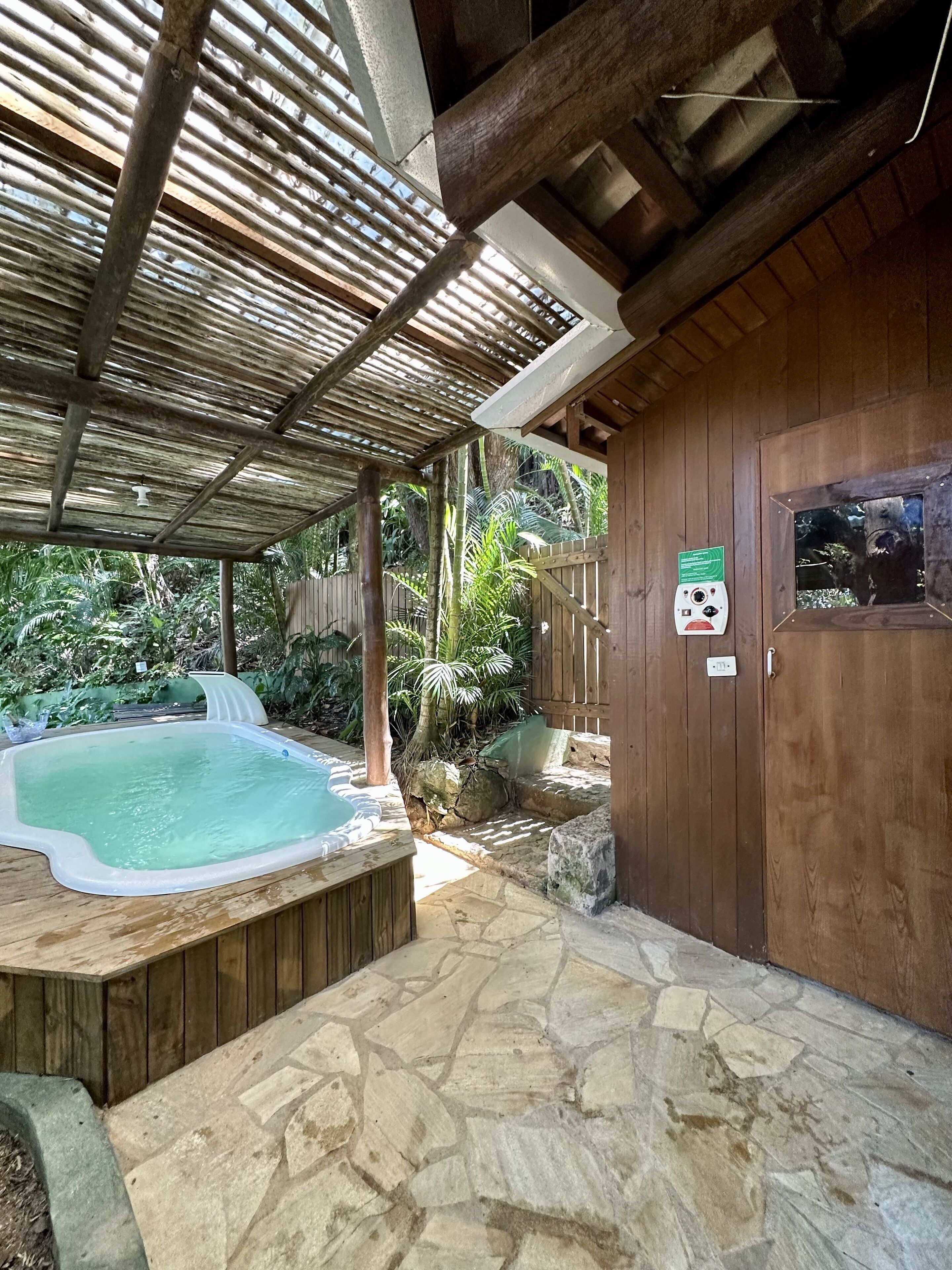 A wooden cabin with a hot tub, stone flooring, and a wooden fence.