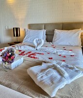 Een hotelkamer met een keurig opgemaakt bed, een bloemenboeket en een decoratieve handdoek in de vorm van een zwaan.