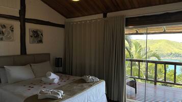 Habitación de hotel con cama, ventilador de techo, ventana con cortinas y vista al paisaje.