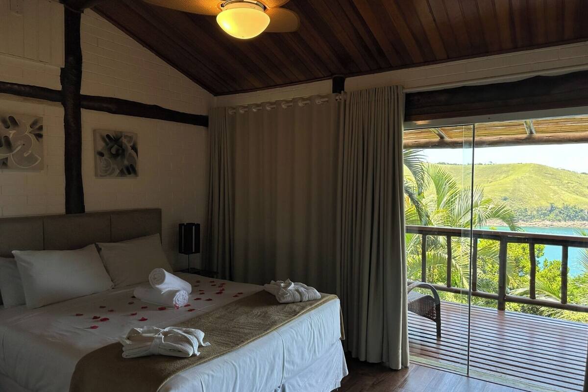 A hotel room with a bed, a ceiling fan, a view of the outdoors, and a window with curtains.
