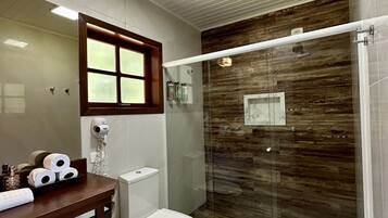 Un baño moderno con ducha de vidrio, inodoro, lavabo con encimera de madera y espejo con ventana arriba.