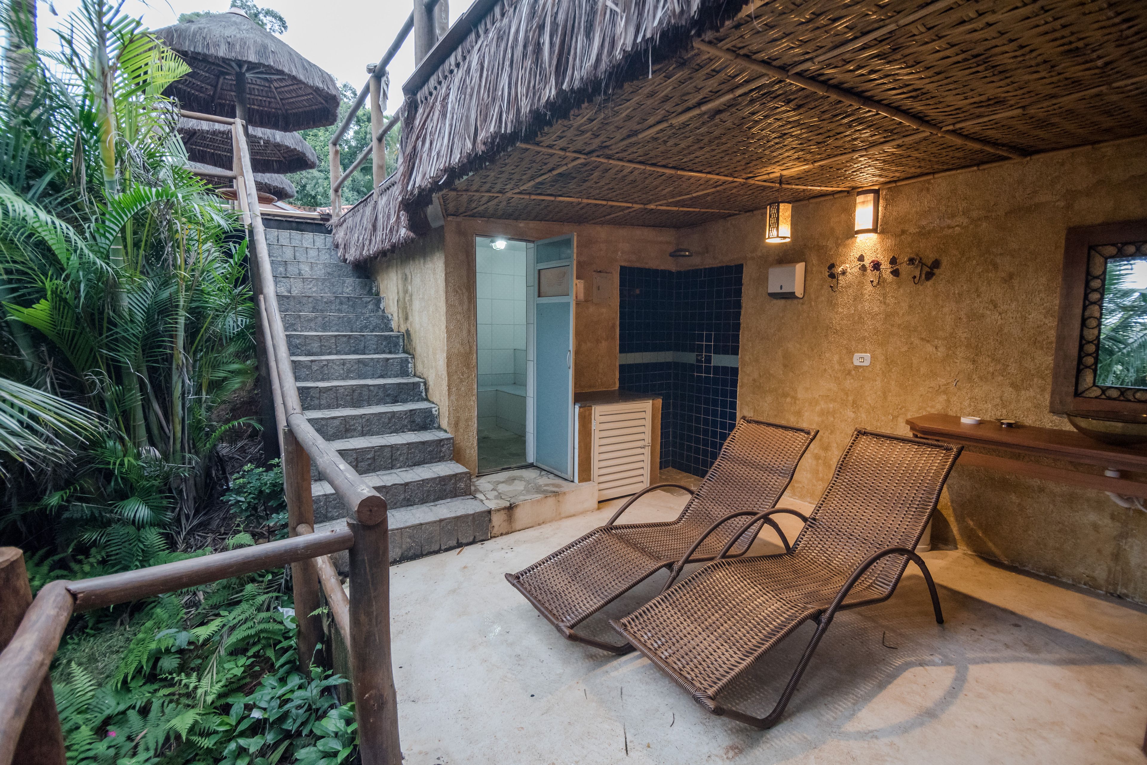 A staircase leading to a room with a thatched roof, a small pool, and two lounge chairs.
