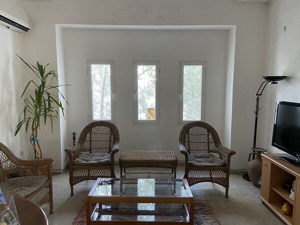A living room with wicker furniture, a glass coffee table, and a television on a wooden stand. - Omar Hotel & Suites (Bodrum)