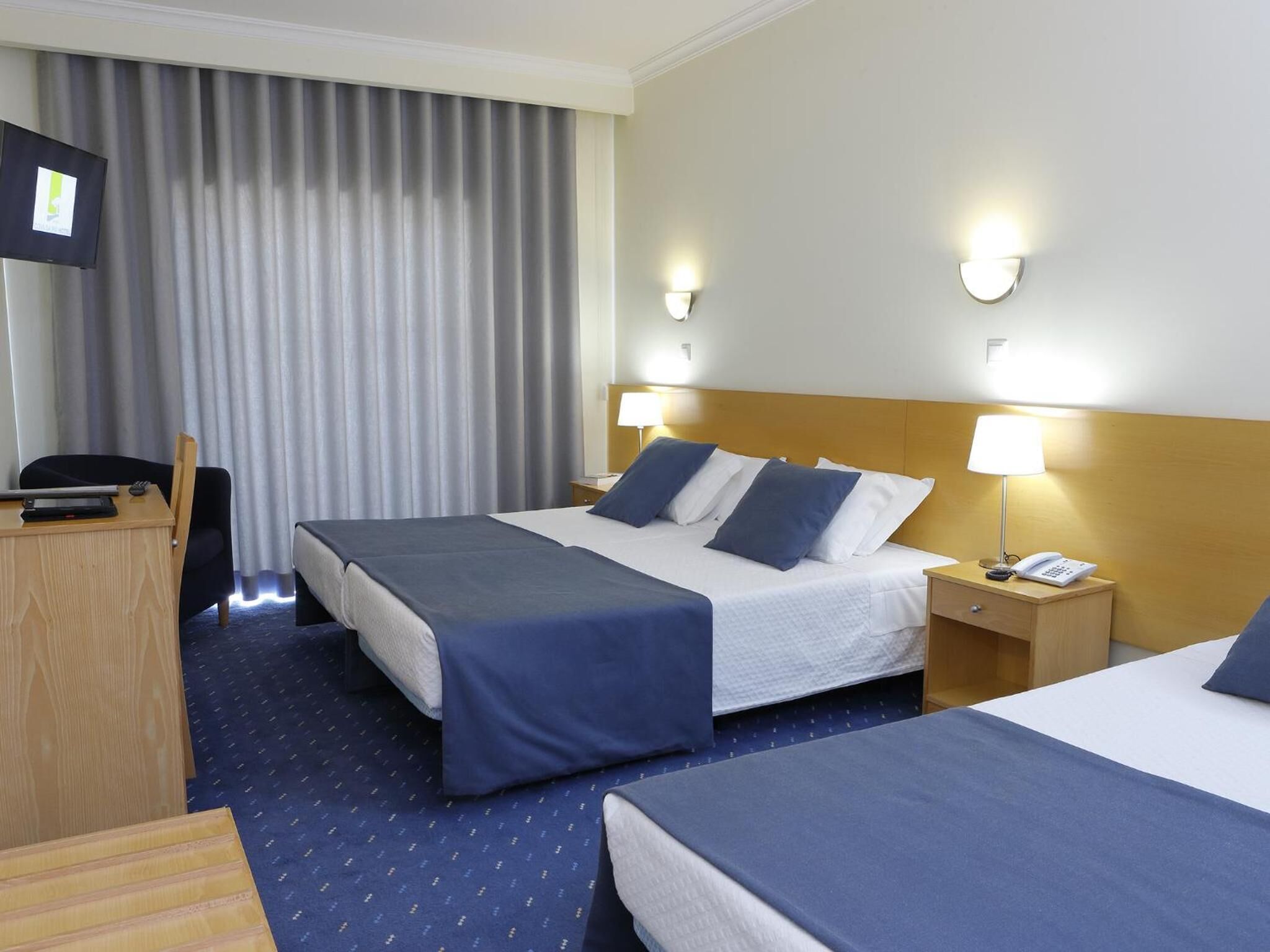 Hotellihuone, jossa on kaksi sänkyä, työpöytä, tuoli ja televisio.
