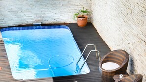 A rectangular swimming pool with a tiled edge, surrounded by a wooden deck. There are two wicker chairs with white cushions and a potted plant nearby. - Signal Hill Lodge (Cape Town)