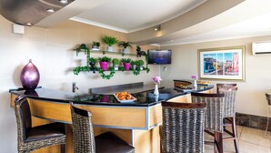 A modern kitchen with a bar area, bar stools, and a television mounted on the wall. - Signal Hill Lodge (Cape Town)