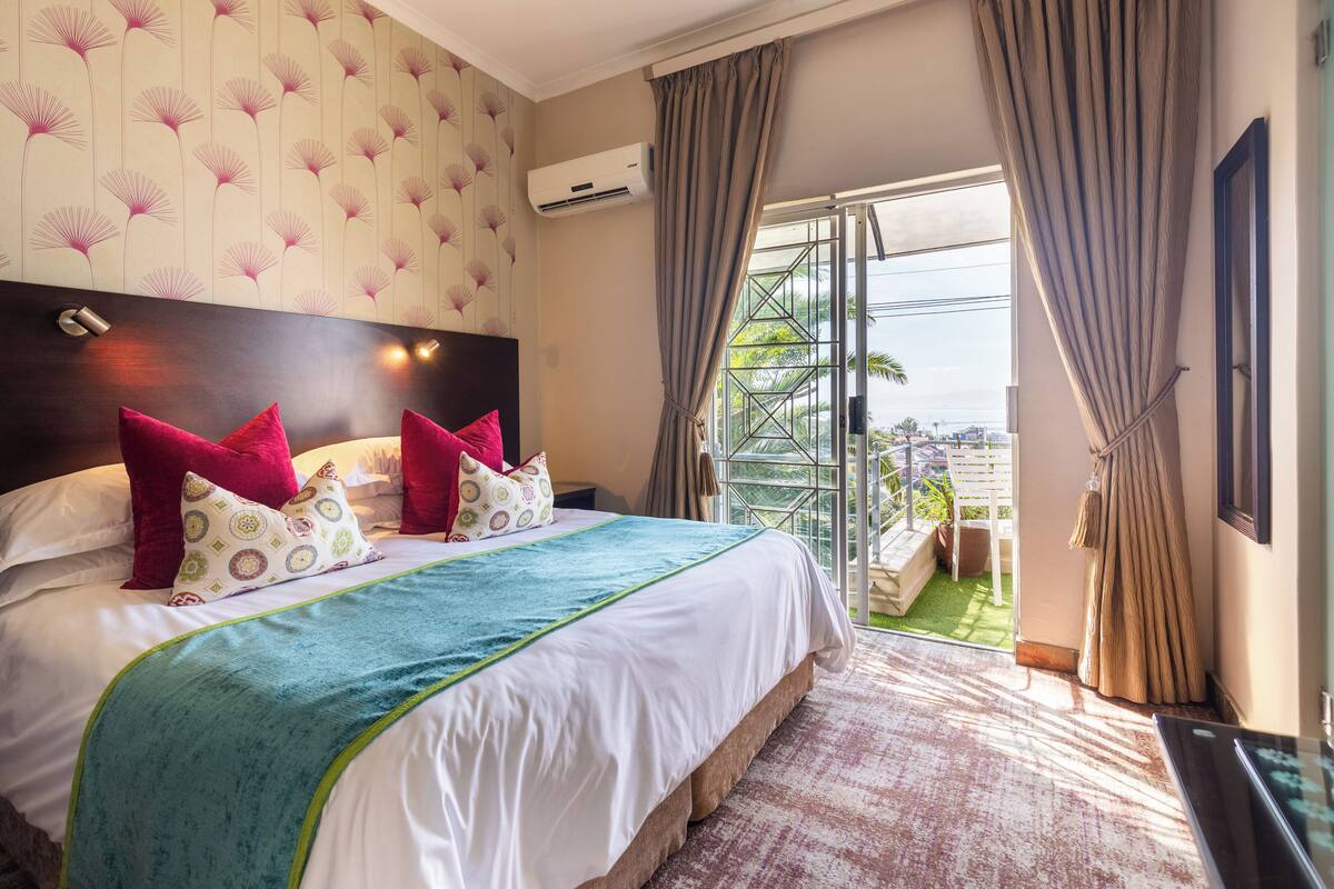 A hotel room with a large bed, a view of the outdoors, and an air conditioning unit on the wall.
