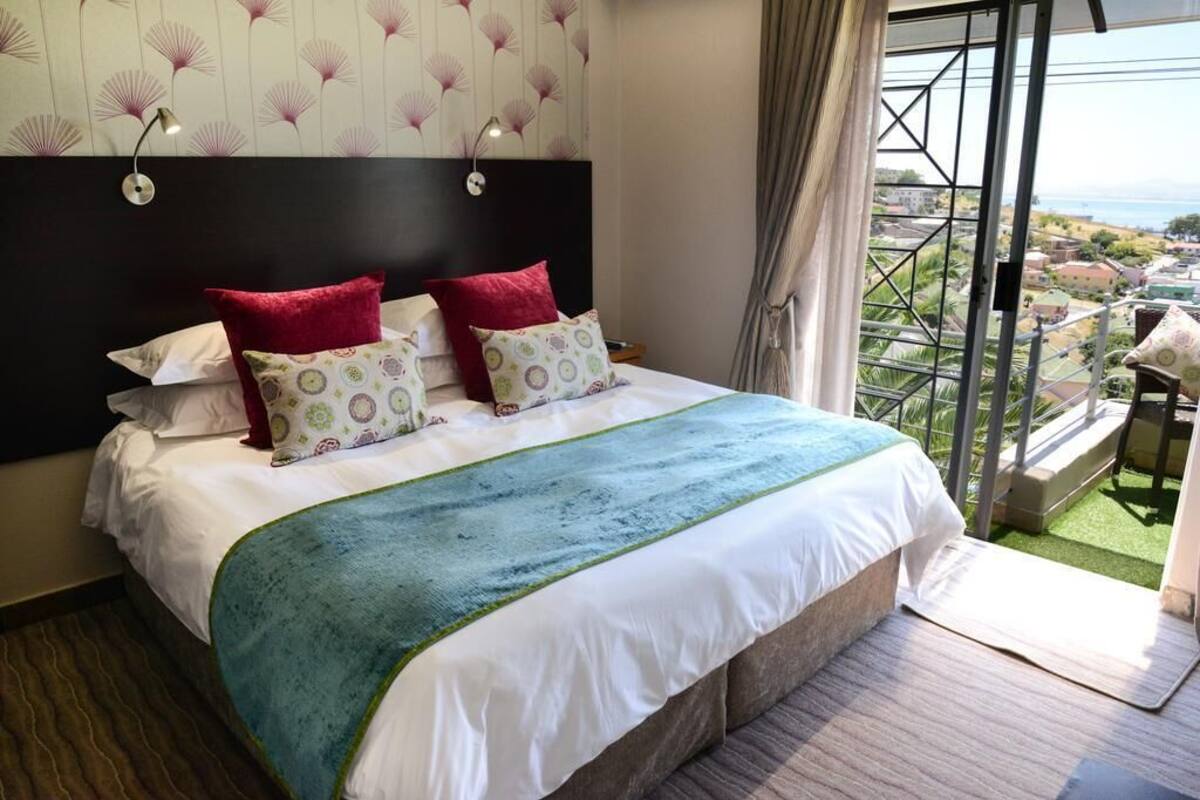 A hotel room with a large bed, a view of the city, and a balcony with a view.