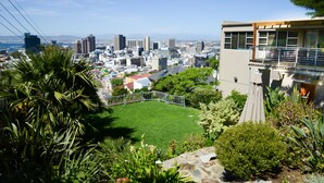 A residential area with a well-maintained lawn, a balcony with a railing, and a view of a cityscape with buildings and a distant body of water. - Signal Hill Lodge (Cape Town)
