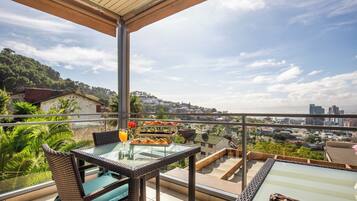 Parveke, jossa on rottinkihuonekaluja, lasipöytä ja näkymä kaupunkiin.