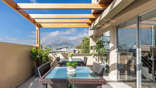 A patio with wicker furniture, glass-top tables, and potted plants. - Signal Hill Lodge (Cape Town)