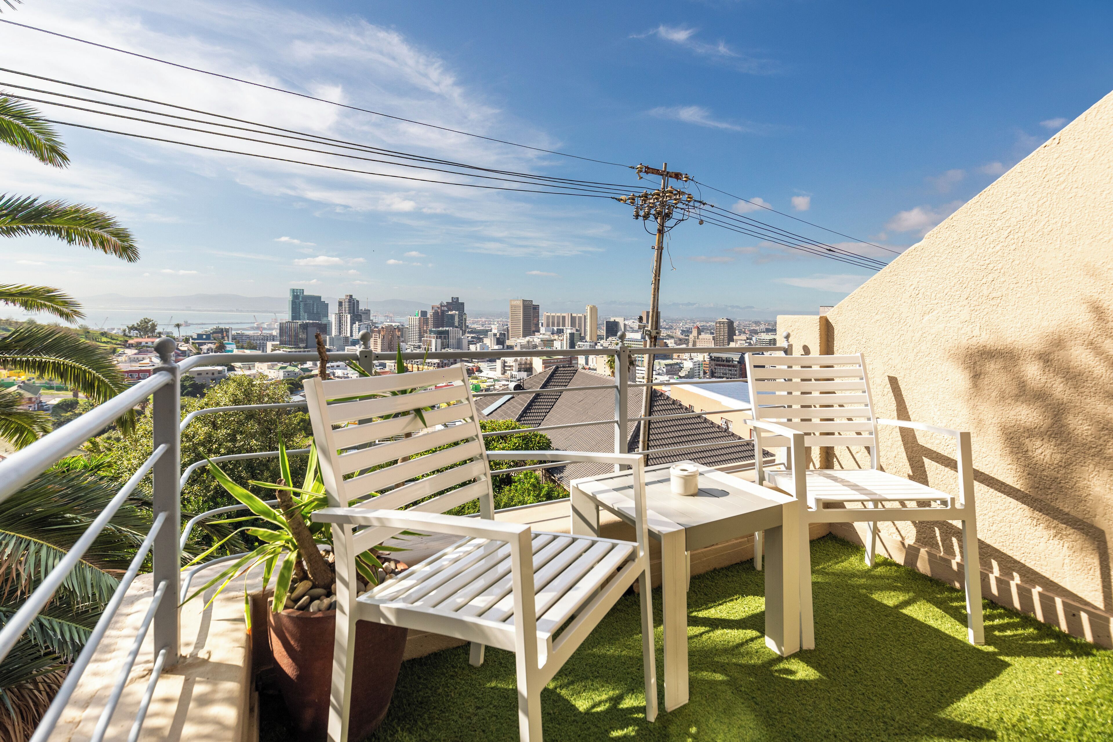 Terraza en la azotea con sillas y mesas blancas, vista del horizonte urbano y una palmera.