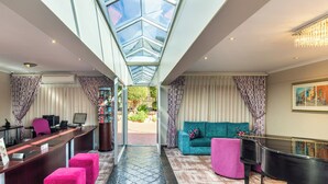 A hotel lobby with a reception desk, a piano, a sofa, and a glass ceiling. - Signal Hill Lodge (Cape Town)