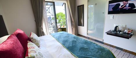Una habitación de hotel con cama, televisión, ventana con cortinas y una mesita con tetera y tazas.