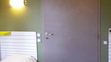 Une chambre d’hôtel avec deux lits, une porte, un climatiseur fixé au mur et un luminaire.