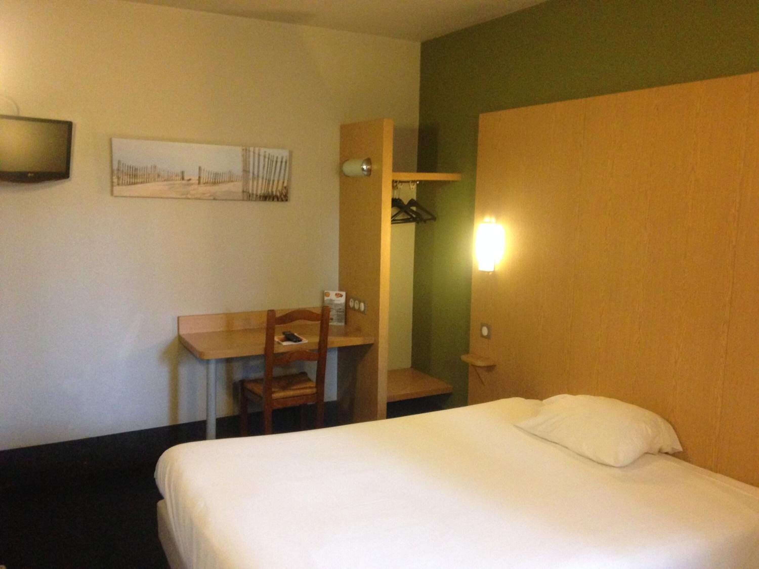 A hotel room with a bed, a desk, a chair, a television, and a wall-mounted light.