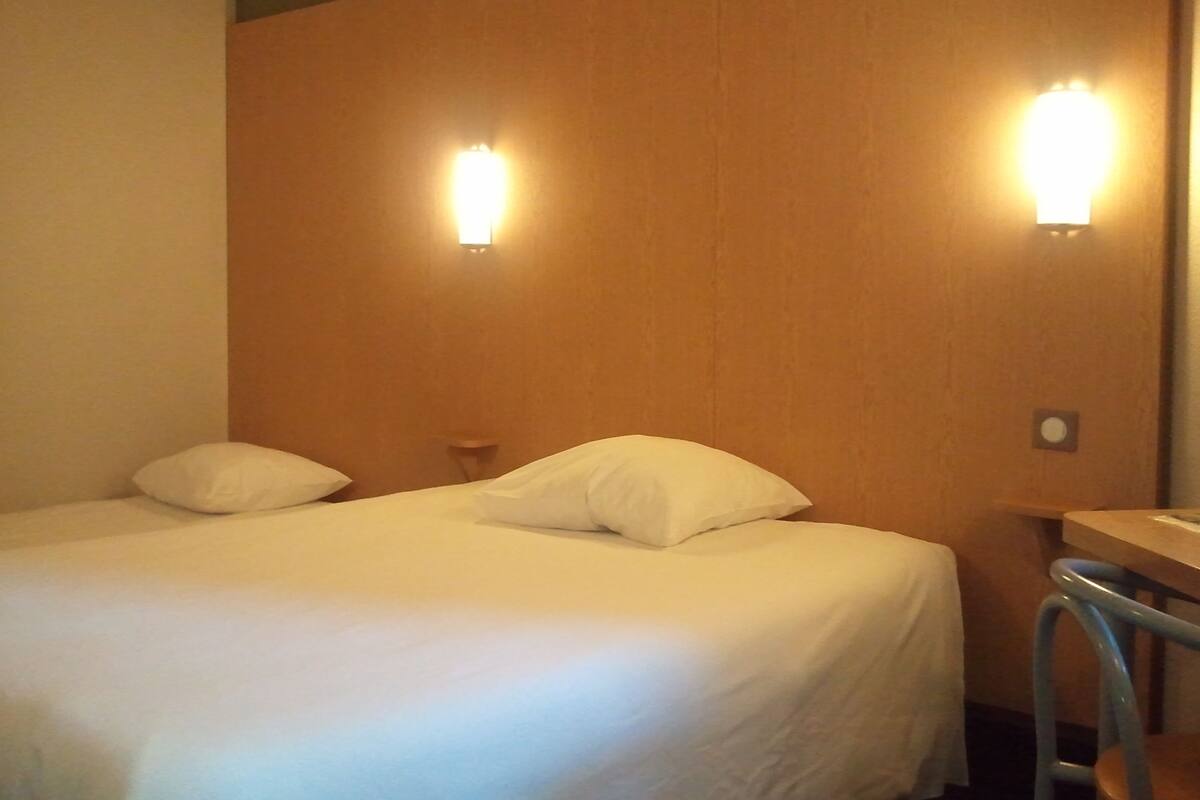 A hotel room with two beds, a wooden headboard, and two wall-mounted lights.
