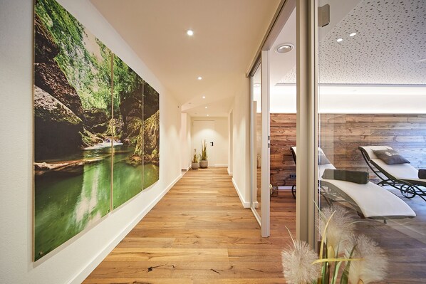 Un pasillo con un gran mural de temática natural, suelo de madera y una zona de estar con vistas al exterior.