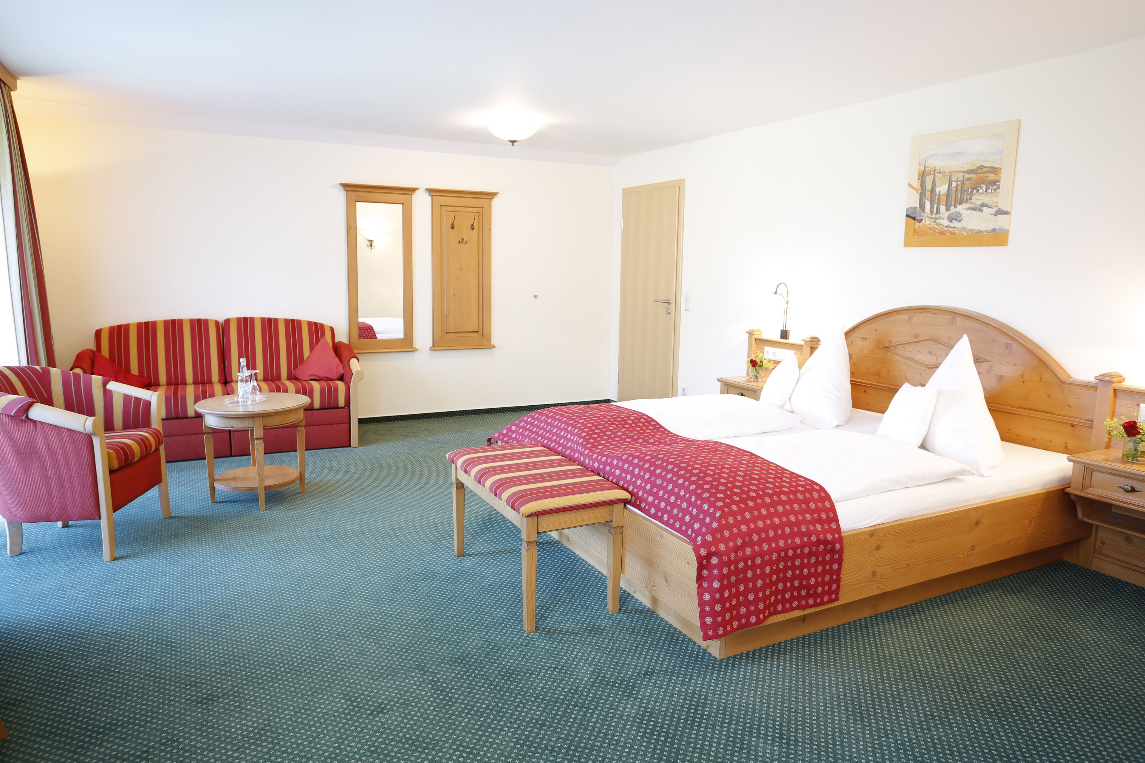 A hotel room with a bed, a bench, a sofa, a small table, and a mirror.