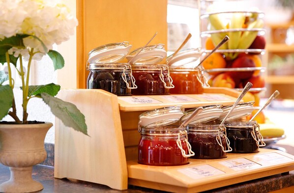 A display of various jams with labels, a potted plant, and a fruit basket in the background. - Landhotel Mohren (Wangen im Allgäu)