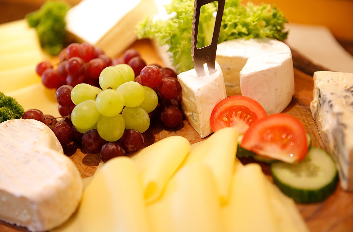 Una selección de quesos y frutas sobre una tabla de madera.