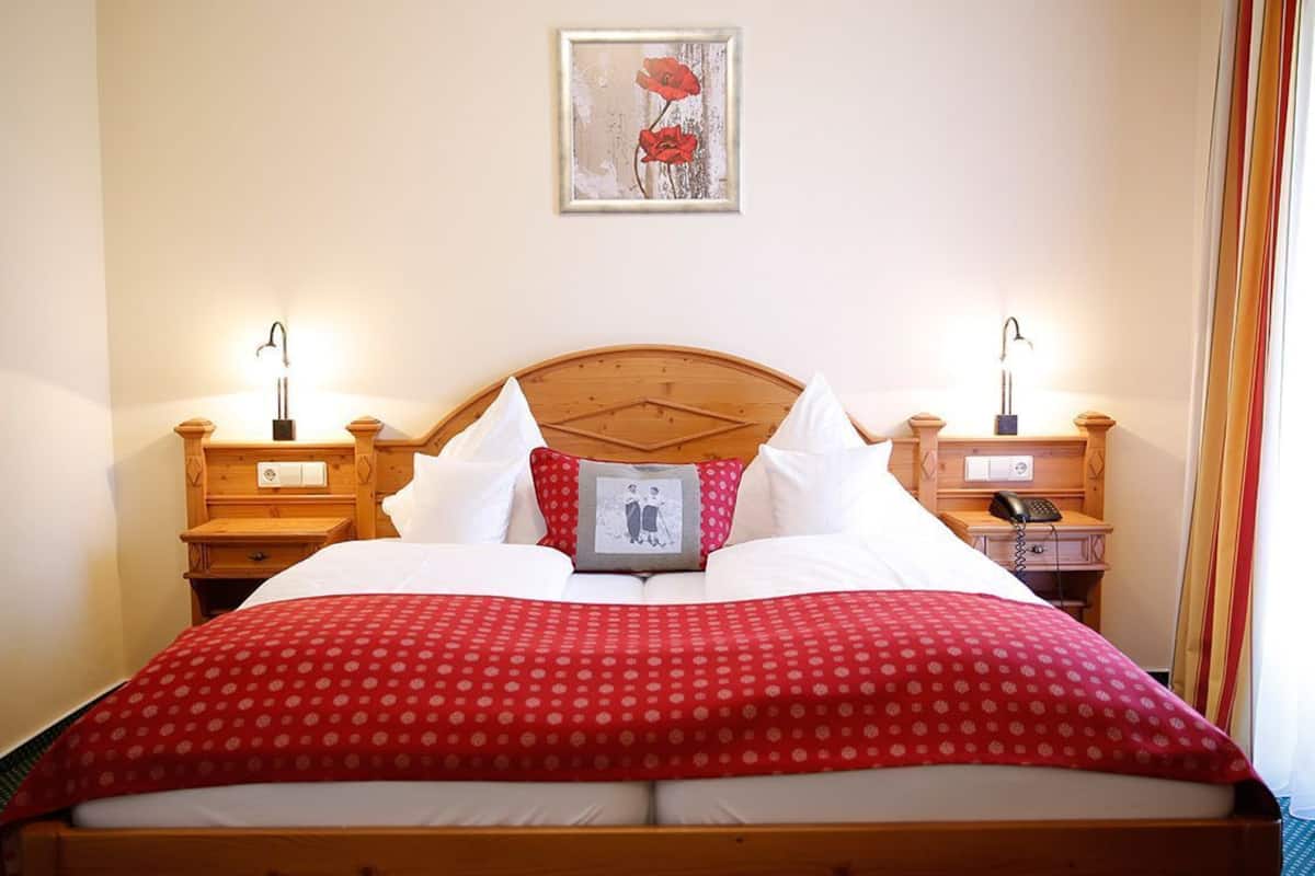 Habitación de hotel con una cama de madera, dos mesitas de noche con lámparas, un cuadro en la pared y un teléfono sobre la mesa de la derecha.