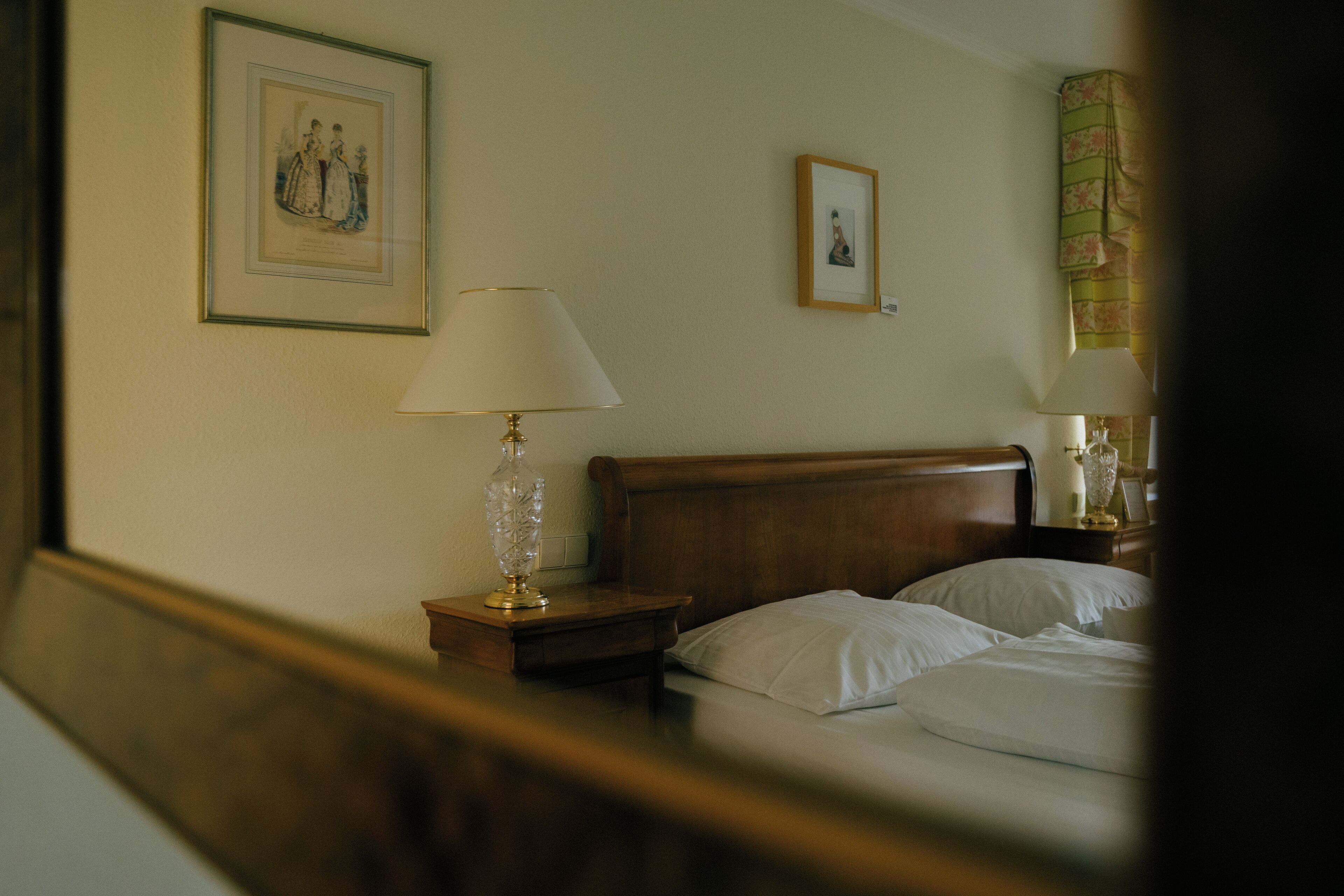 Una habitación de hotel con cabecera de madera, una mesita de noche con lámpara y un cuadro enmarcado en la pared.