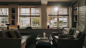 A cozy living room with a leather sofa, armchairs, a glass coffee table, and a bookshelf. - Hotel Restaurant Mühle (Binzen)