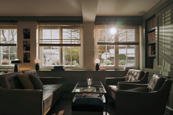 A cozy living room with a leather sofa, armchairs, a glass coffee table, and a bookshelf. - Hotel Restaurant Mühle (Binzen)