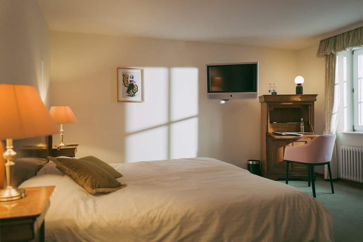 A hotel room with a bed, a desk, a chair, a television, and a picture on the wall.