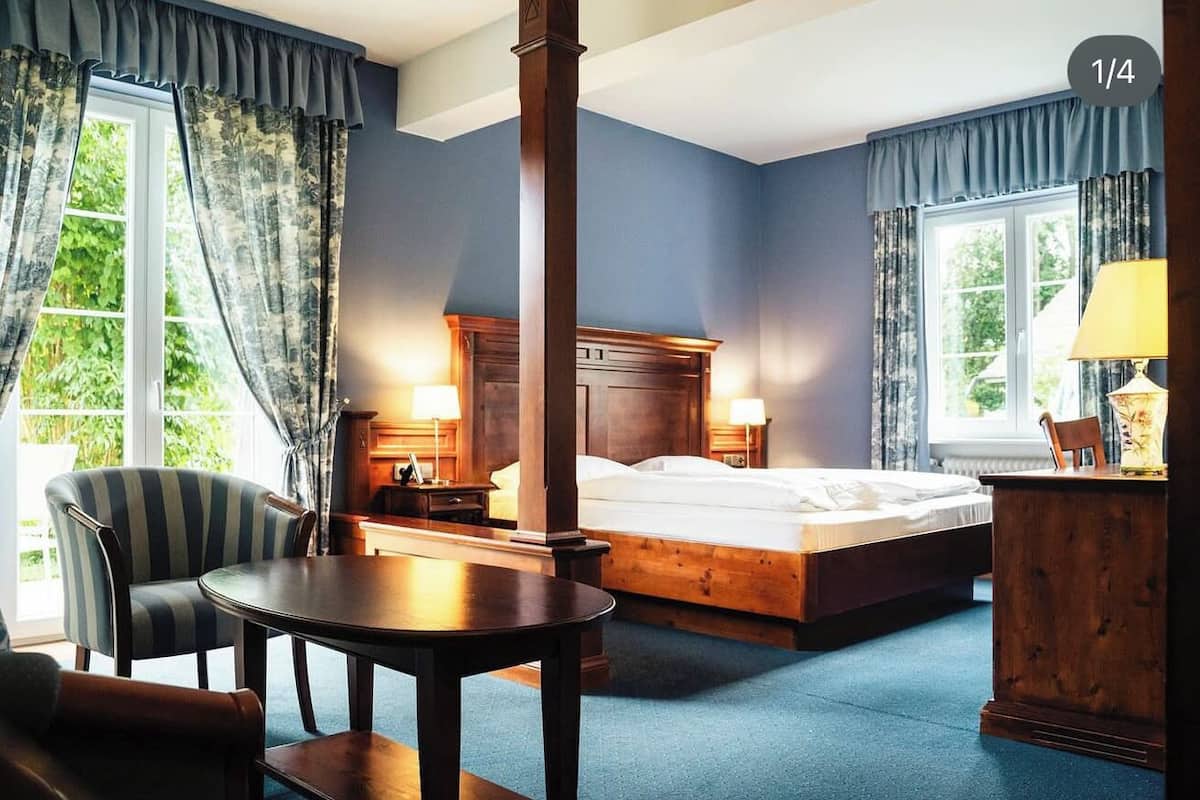 A hotel room with a bed, a wooden headboard, a round table, a chair, a desk, and a lamp.