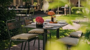 An outdoor dining area with metal chairs and tables, a vase with flowers, and a lamp. - Hotel Restaurant Mühle (Binzen)