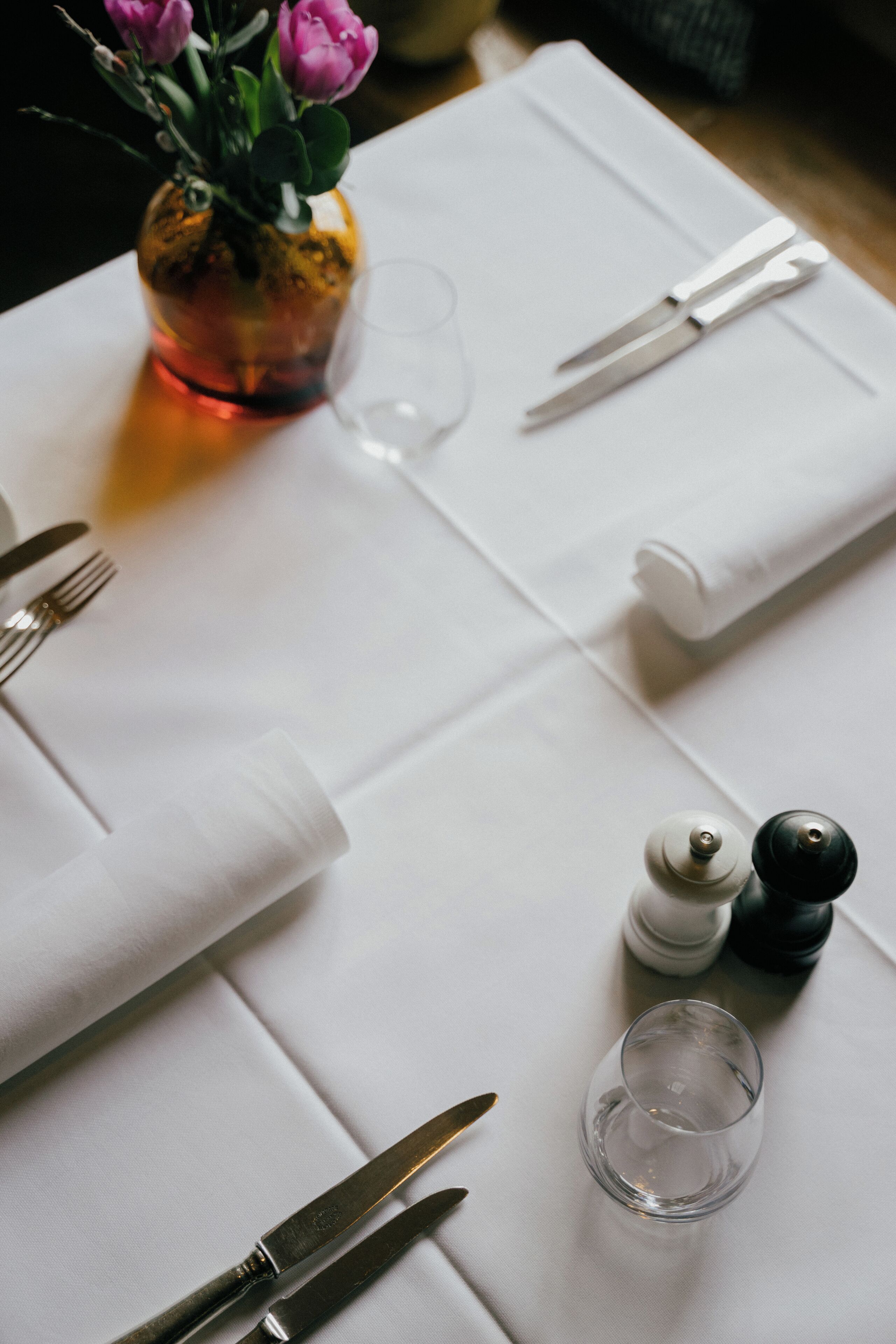 A neatly arranged table with a white tablecloth, a clear glass, a salt and pepper shaker, and a small vase with flowers.
