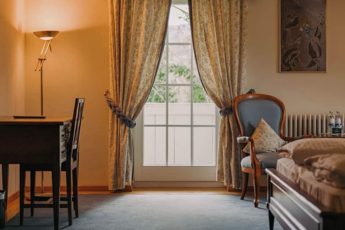 A bedroom with a bed, a chair, a desk, and a window with curtains.