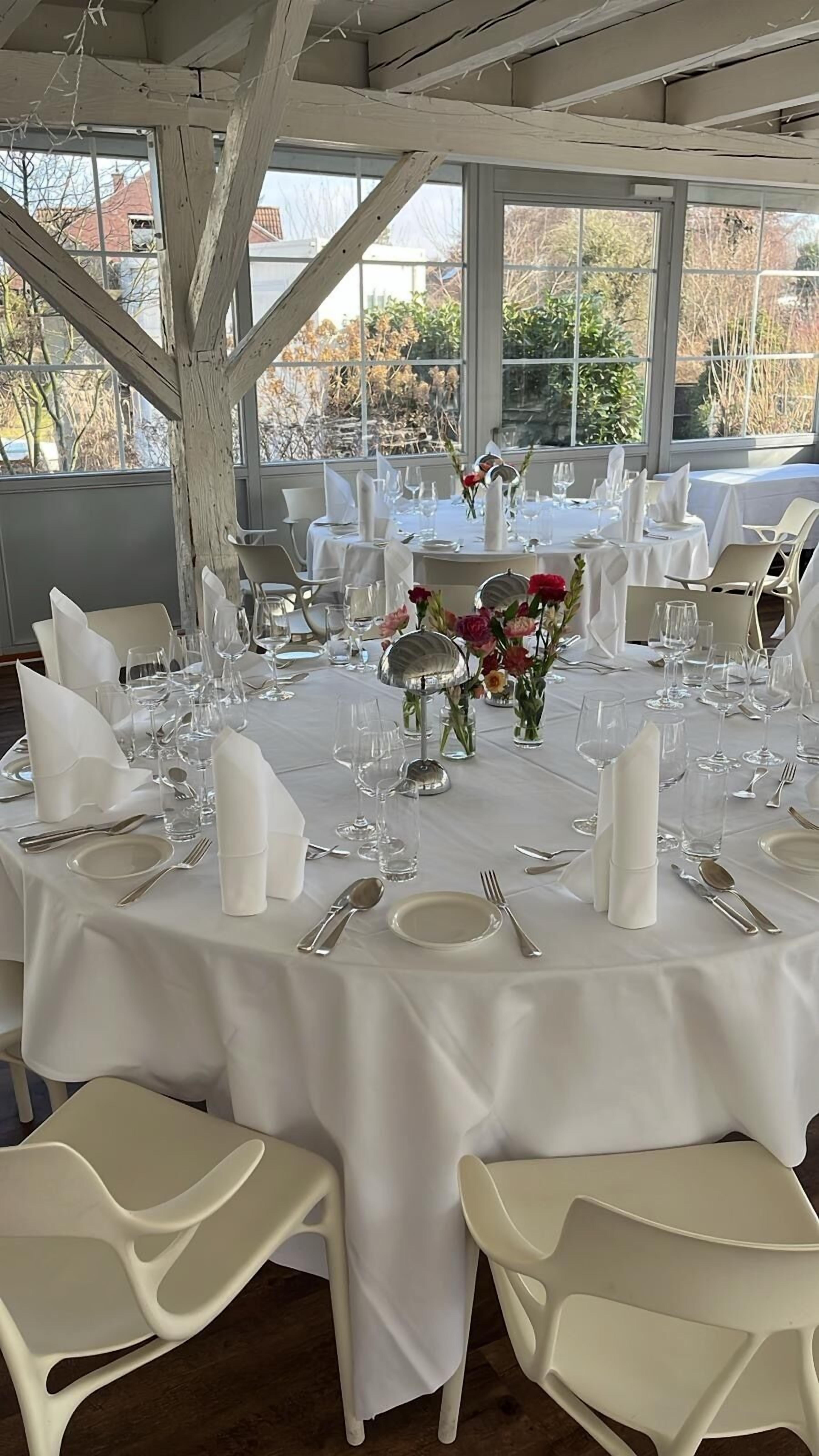 Une table ronde dressée pour un événement formel, avec des nappes blanches, des couverts en argent et de la verrerie élégante.