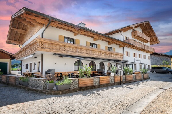 Traditional Alpine-style building with a balcony and wooden beams, offering outdoor seating and a charming atmosphere.