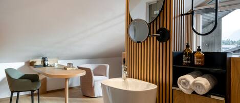 A modern bathroom with a wooden vanity, a round mirror, a sink, and a shelf with towels and toiletries.