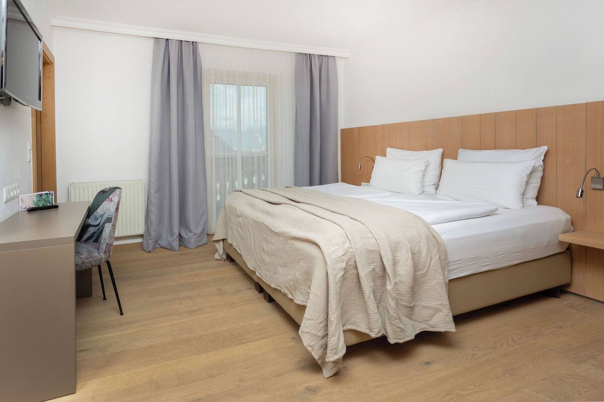 A modern hotel room with a large bed, a desk, and a television.