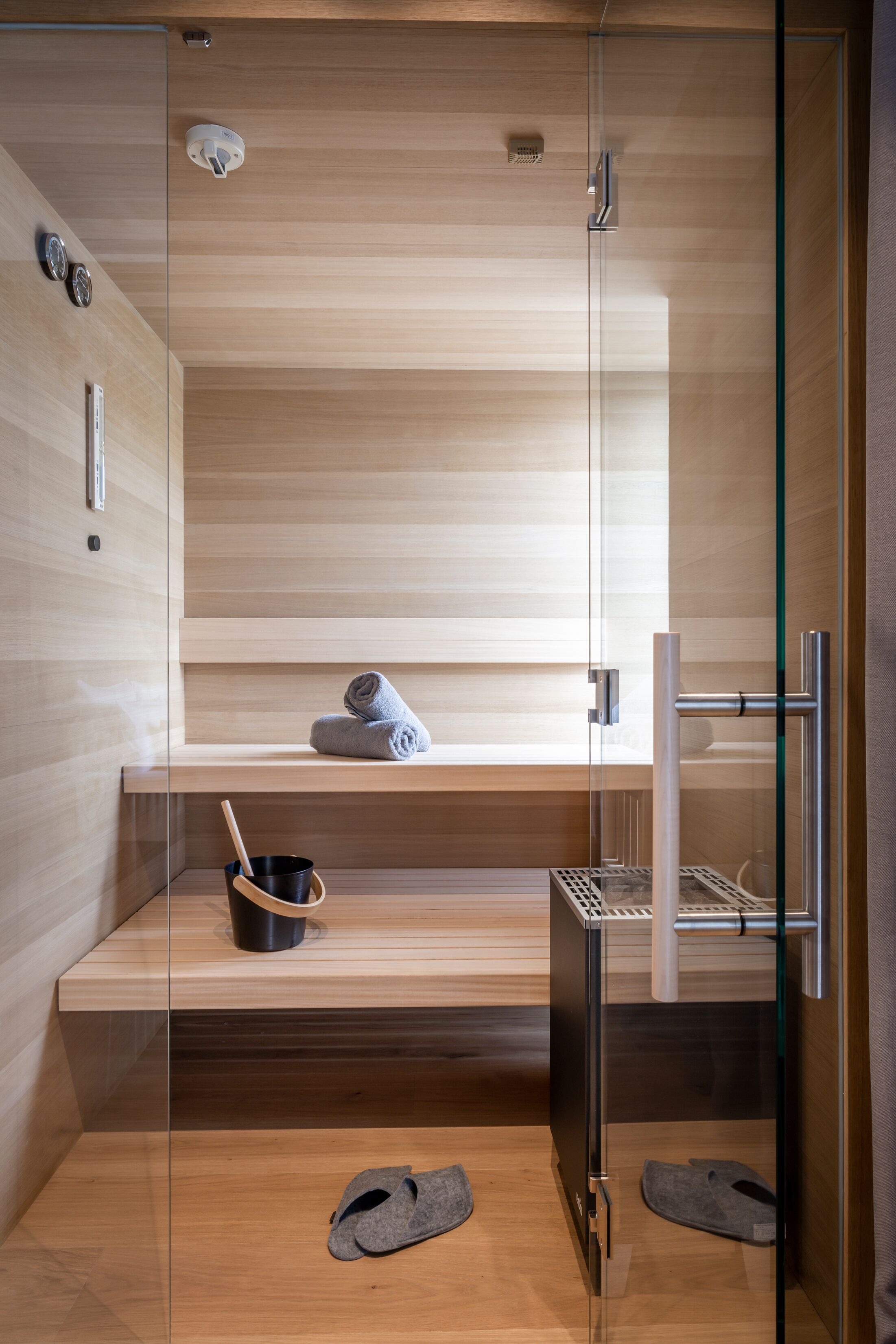 Eine moderne Sauna mit Glaswänden, Holzbänken und einem Metallregal.